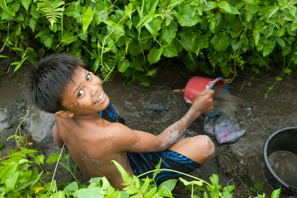 Poor kid catches small fish in a ditch near a rice field — Stock Photo, Image