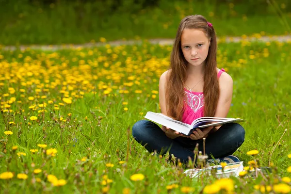 Egy 11 éves lány elolvassa a könyvet, a réten — Stock Fotó