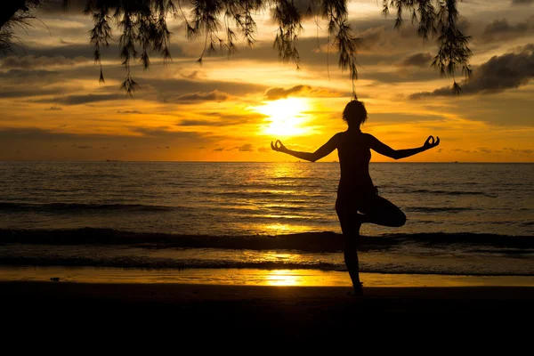 Jovem praticando ioga na praia ao pôr do sol. — Fotografia de Stock