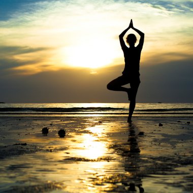 Gün batımında plajda yoga yapan genç bir kadın..