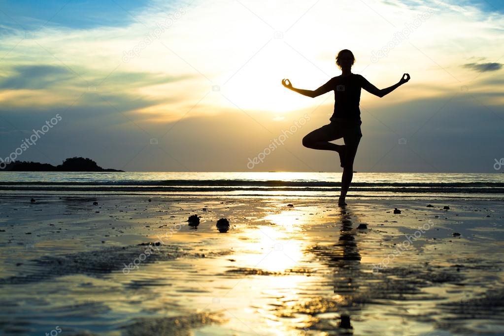 Young woman practicing yoga on the beach at sunset