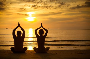Young couple practicing yoga on the sea beach at sunset
