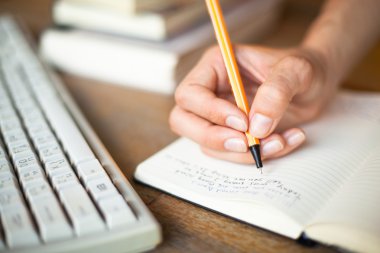 bir dizüstü bilgisayar, bilgisayar klavye ve bir yığın kitap arka planda bir kalem eller fotoğraf yazıyor