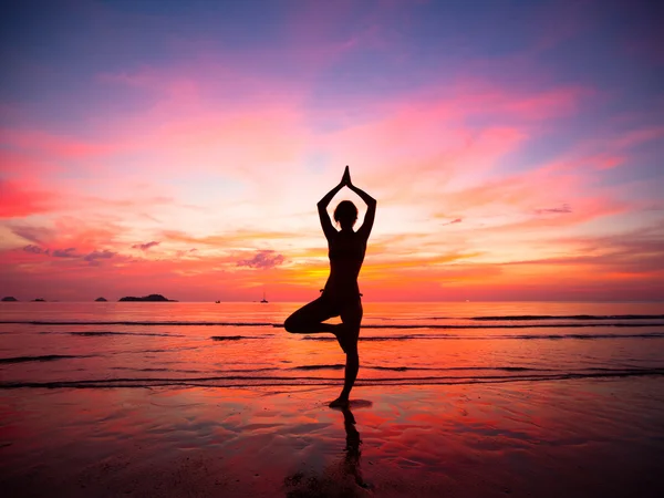 Silhuetten av en vacker yoga kvinna på kvällen på stranden vid solnedgången — Stockfoto