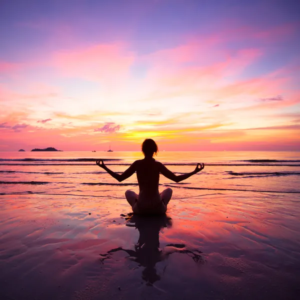 Uma mulher praticando ioga sentado na praia durante o pôr do sol — Fotografia de Stock