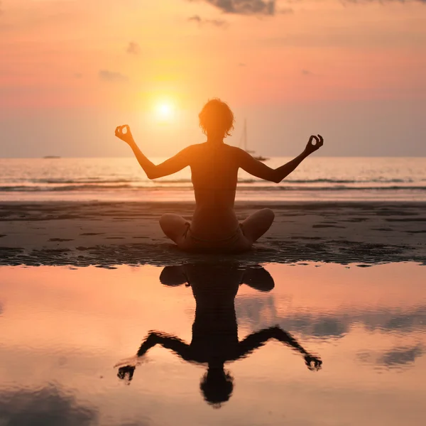 Silhuetten av en vacker yoga kvinna på stranden vid solnedgången — Stockfoto