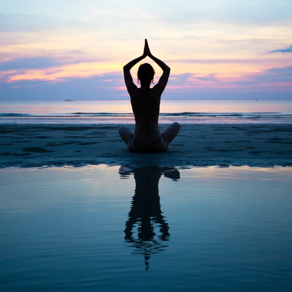 Silueta de una mujer yoga sobre la puesta de sol del mar con reflejo en el agua —  Fotos de Stock