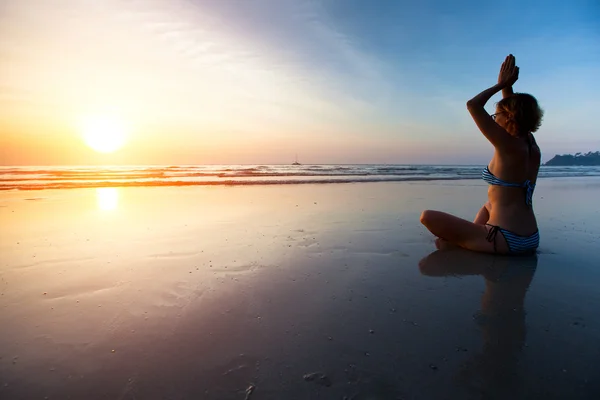 Jóga žena sedí na pobřeží moře při západu slunce. — Stock fotografie