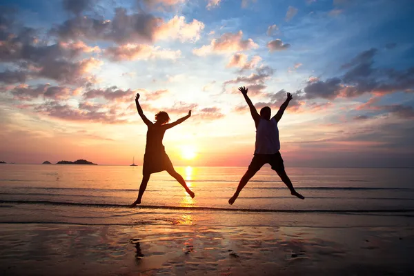 Concept van de langverwachte vakantie: jong koppel in een sprong op de zee strand bij zonsondergang. Stockfoto