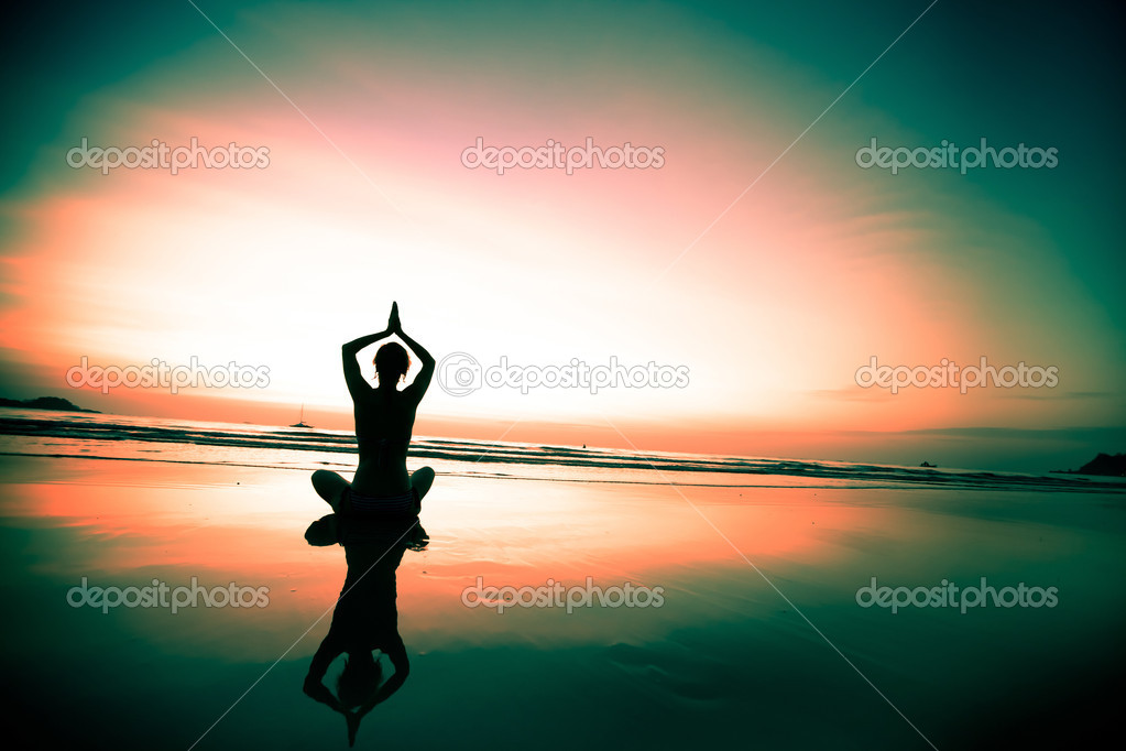 Woman meditating on the beach at sunset