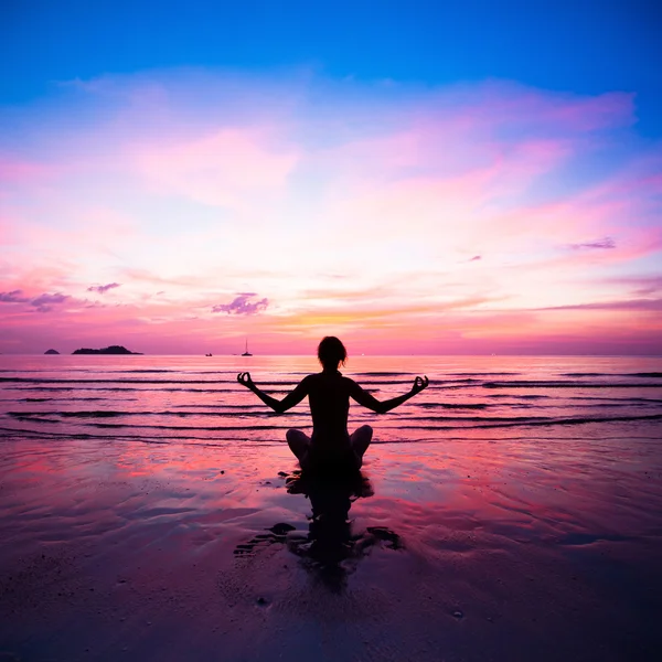 Jonge vrouw oefenen yoga op het strand bij zonsondergang. Stockfoto