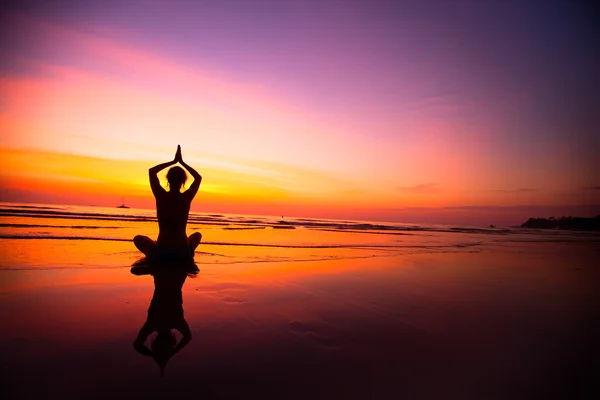 Silueta de mujer practicando yoga en la playa durante una hermosa puesta de sol . — Foto de Stock