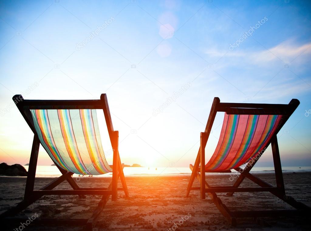 Vacation concept: Pair of beach loungers on the deserted coast sea at sunrise.