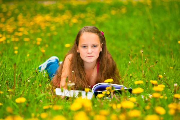 Lilla flickan läsa en bok liggande i gräset — Stockfoto