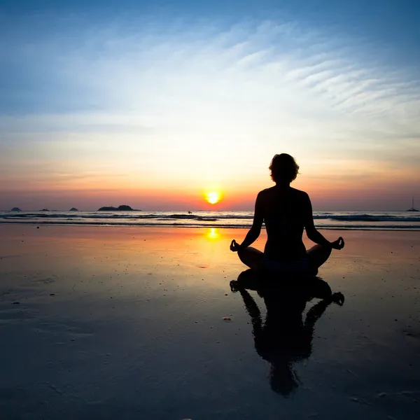 Silhouette yoga donna seduta sulla costa del mare al tramonto . — Foto Stock