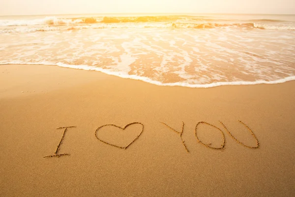 Eu te amo - texto escrito à mão na areia em uma praia, com uma onda azul . — Fotografia de Stock