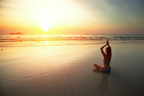 Junge Frau meditiert am Strand bei Sonnenuntergang. — Stockfoto