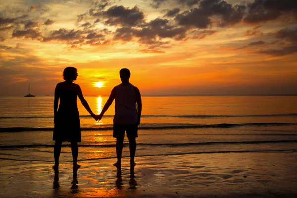 Imagen romántica: Siluetas pareja joven en la playa al atardecer . — Foto de Stock