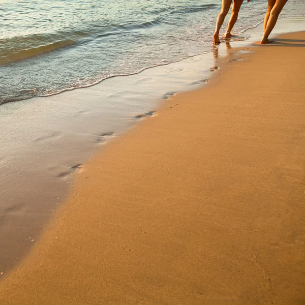 Fotspår på stranden kvar bakom par promenader längs sandstranden, mjuk våg av havet — Stockfoto