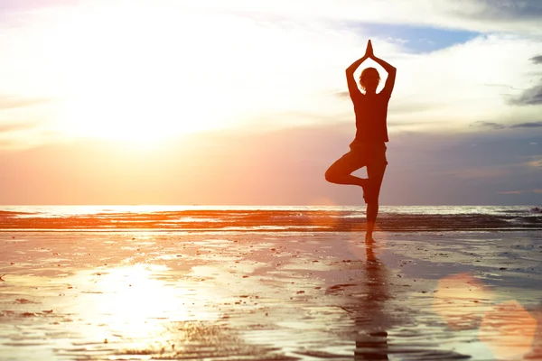 Gün batımında plajda yoga yapan genç bir kadın. — Stok fotoğraf