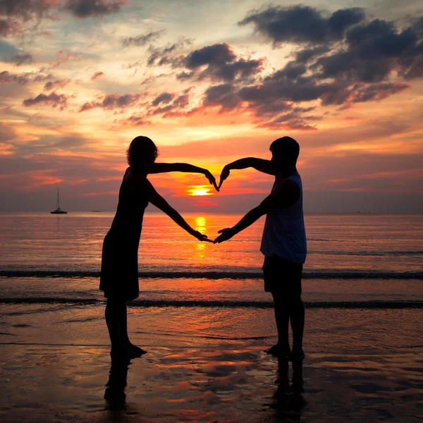 Pareja joven cogida de la mano en forma de corazón en la playa del mar al atardecer . — Foto de Stock