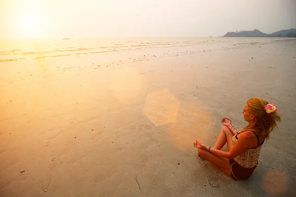 日没にビーチでヨガを練習している若い女性が — ストック写真