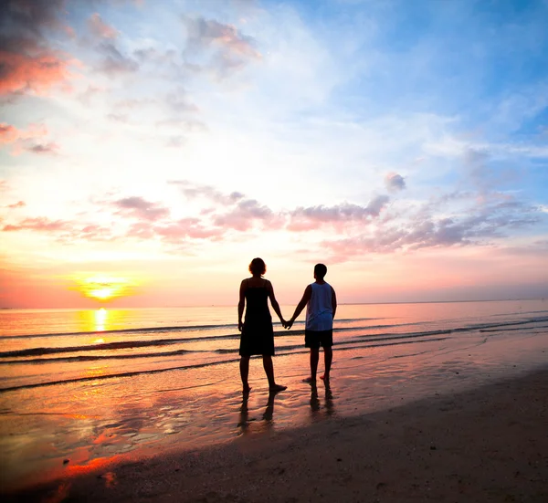 Junges Paar hält Händchen am Strand bei Sonnenuntergang. — Stockfoto