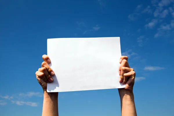 Mani che tengono pulito foglio di carta bianca sopra il cielo . — Foto Stock