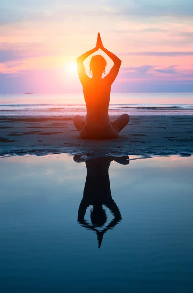Mladá žena cvičí jógu na pláži při západu slunce Stock Snímky