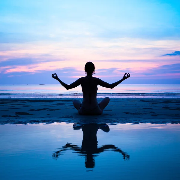 Silueta de una mujer yoga sobre la puesta de sol del mar con reflejo en el agua —  Fotos de Stock