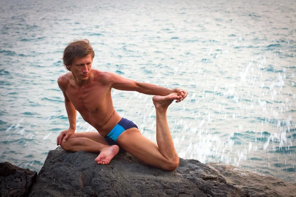 Młody człowiek robi ćwiczenia jogi na plaży opuszczonej dziki kamień nad morzem — Zdjęcie stockowe