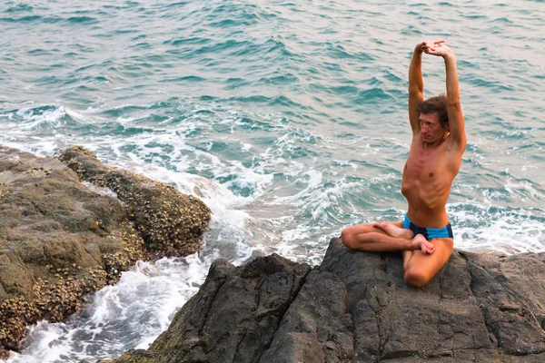 Young man doing yoga exercise in the lotus position on the deserted wild stone sea beach — Stock Photo, Image