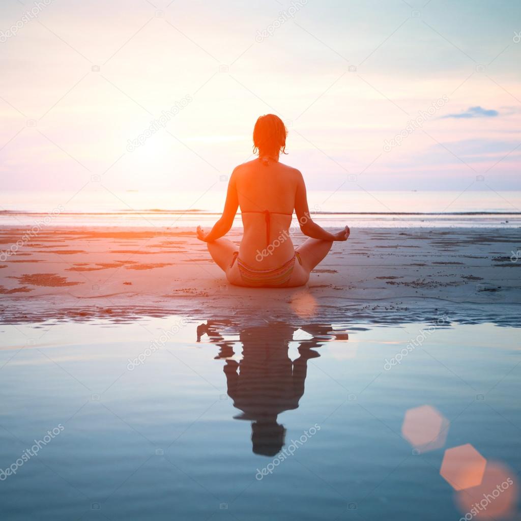 Woman practicing yoga on the beach at sunset, with reflection in water