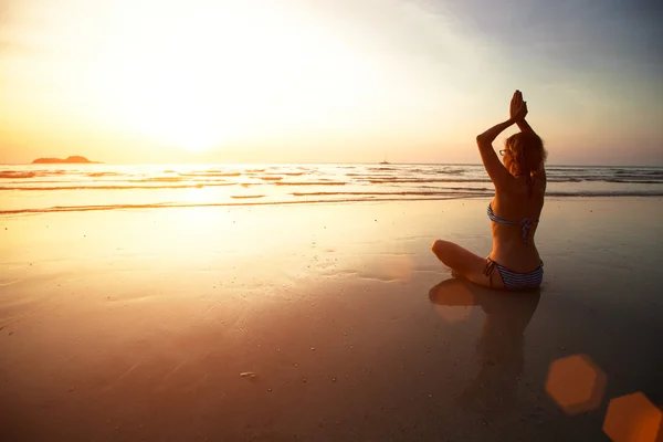 Jóga nő ül a tengerparton naplementekor. — Stock Fotó