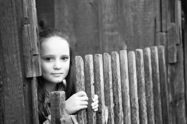 Dospívající dívka stojící poblíž historických venkovských plot, černobílé fotografie. — Stock fotografie