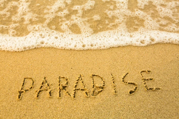 Paradiso - scritto in sabbia sulla texture della spiaggia - morbida onda del mare — Foto Stock