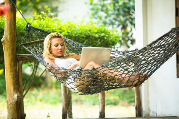 Mujer joven se encuentra en la hamaca con el ordenador portátil — Foto de Stock