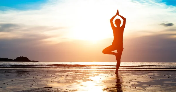 Jonge vrouw silhouet beoefenen van yoga op het strand — Stockfoto