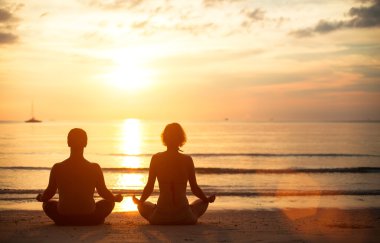 A young couple sitting on the beach of the sea in the lotus position