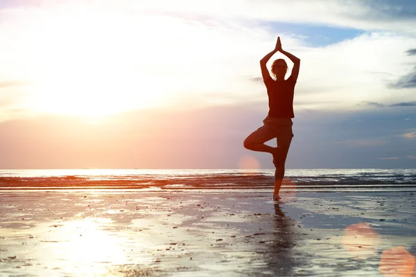 Cvičí jógu na pláži při západu slunce — Stock fotografie
