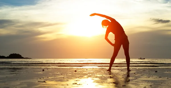 Silhouet jonge vrouw, oefening op het strand bij zonsondergang. Rechtenvrije Stockfoto's