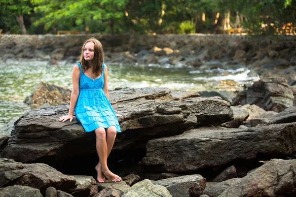 Teen-girl in a blue dress in the rocks of the coast. — Stock Photo, Image