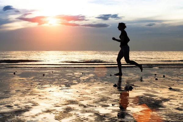 Силуэт молодой женщины бегущей трусцой на закате на берегу моря — стоковое фото
