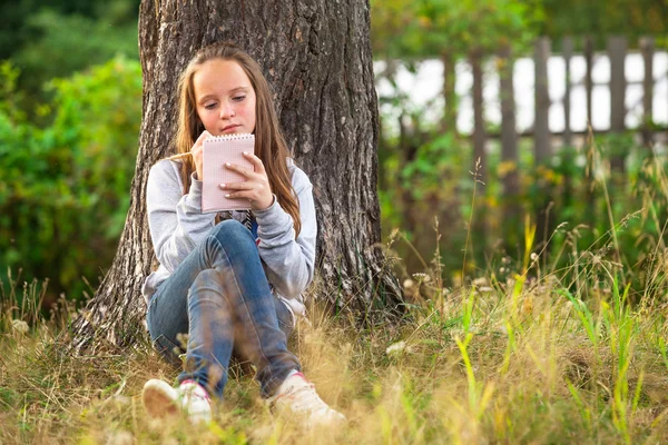 Flicka skriver i en anteckningsbok medan du sitter i parken — Stockfoto