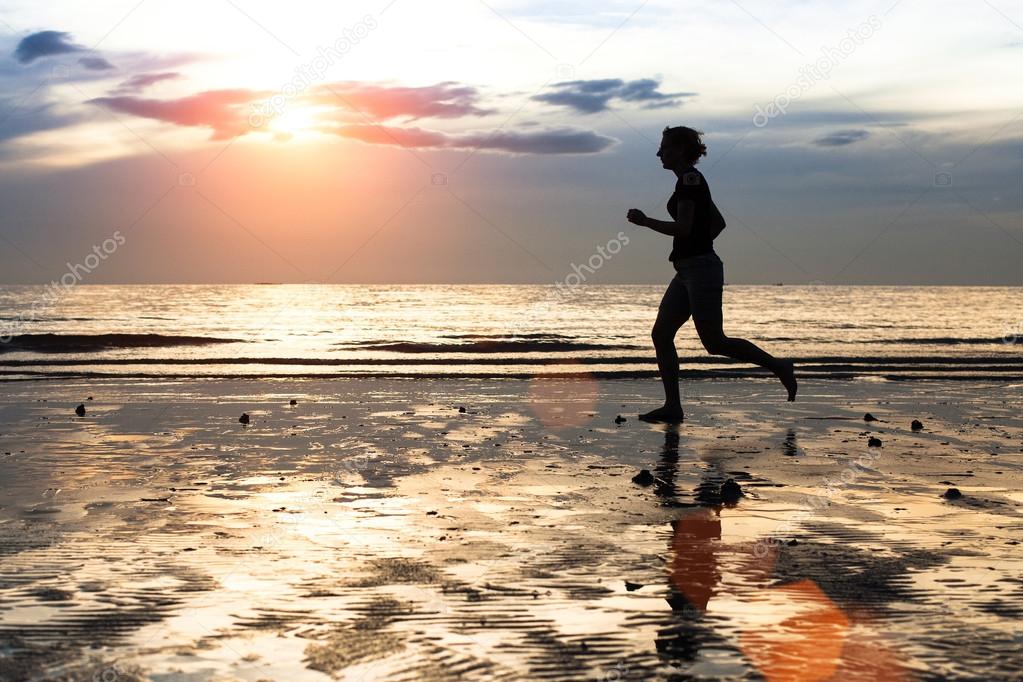 Silhouette of a young woman jogger at sunset on seashore