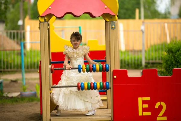 Ei lita jente i elegant kjole på lekeplassen – stockfoto
