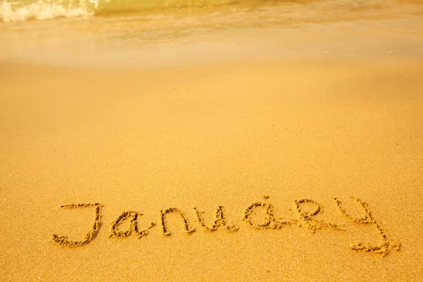 Gennaio - scritto in sabbia sulla spiaggia, morbida onda del mare — Foto Stock