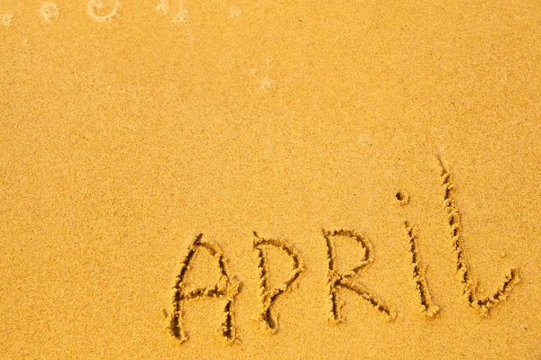 April - geschrieben in Sand auf Strand Textur, weiche Welle des Meeres. — Stockfoto