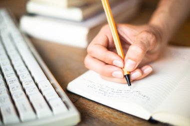 Woman hands writes a pen in a notebook, computer keyboard in background.