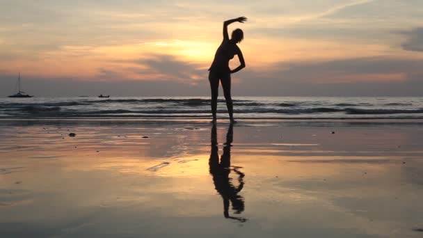 Jonge vrouw presteert oefeningen op het strand tijdens zonsondergang. — Stockvideo